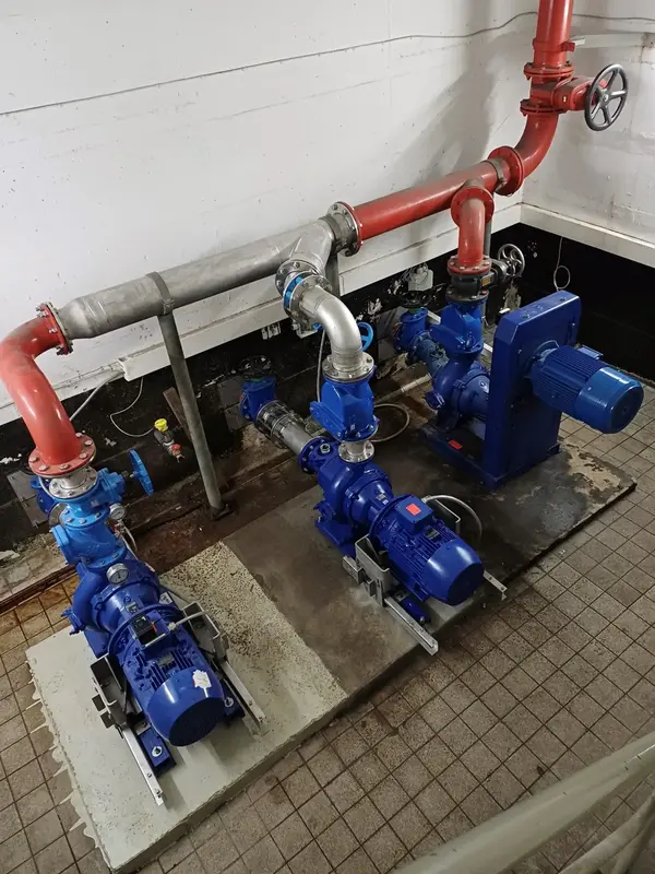 In industrieller Umgebung sind mehrere blaue Pumpen mit Edelstahlrohren sichtbar, die für Rohrleitungsbau eingesetzt werden.