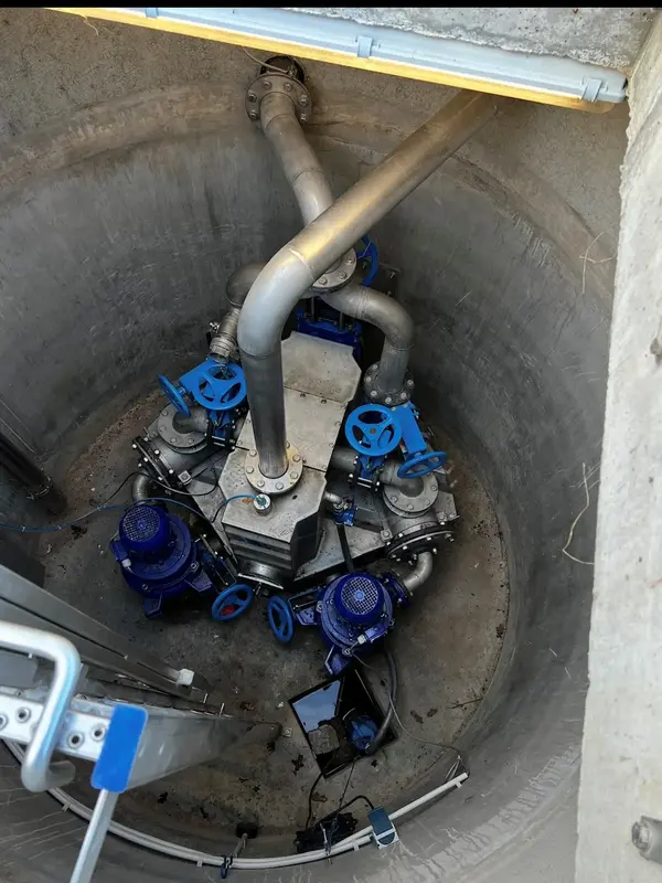 Eine Pumpstation mit blauen Pumpen und Rohren ist in einem runden Schacht sichtbar, bereit für den Rohrleitungsbau.