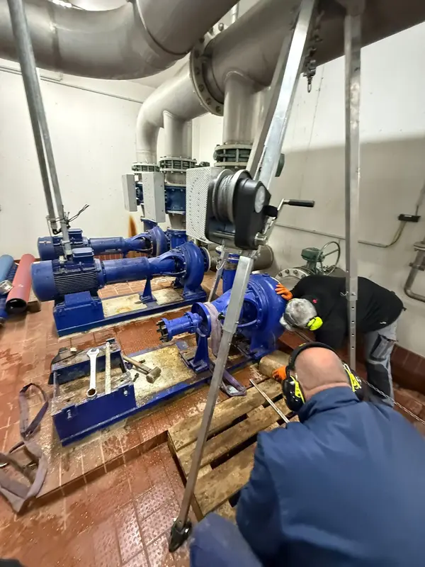 Techniker führen in einem Abwasserwerk Wartungsarbeiten an blauen Pumpen und Rohrleitungen durch, was die Pumpentechnik optimiert.